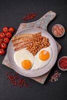 English breakfast with fried eggs, bacon, beans, tomatoes, spices and herbs photo