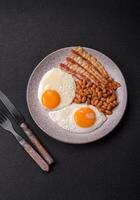 English breakfast with fried eggs, bacon, beans, tomatoes, spices and herbs photo