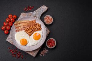 English breakfast with fried eggs, bacon, beans, tomatoes, spices and herbs photo