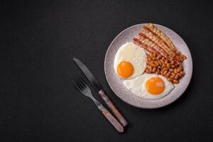 English breakfast with fried eggs, bacon, beans, tomatoes, spices and herbs photo