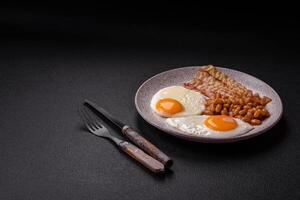 English breakfast with fried eggs, bacon, beans, tomatoes, spices and herbs photo
