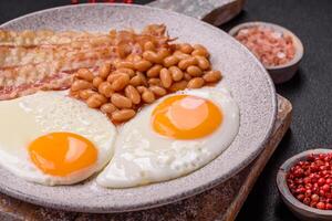 English breakfast with fried eggs, bacon, beans, tomatoes, spices and herbs photo