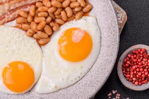 English breakfast with fried eggs, bacon, beans, tomatoes, spices and herbs photo