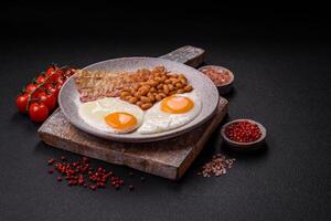 English breakfast with fried eggs, bacon, beans, tomatoes, spices and herbs photo
