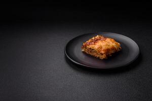 Delicious baked lasagna pasta with meat, sauce, salt, spices and herbs on a dark concrete background photo