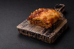 Delicious baked lasagna pasta with meat, sauce, salt, spices and herbs on a dark concrete background photo