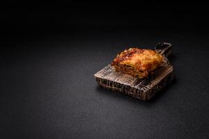 Delicious baked lasagna pasta with meat, sauce, salt, spices and herbs on a dark concrete background photo