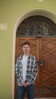 Casual man in front of a wooden door and green wall with urban architecture in the background video