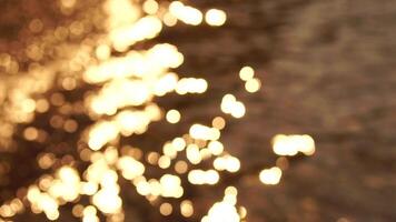 Abstract sea summer ocean sunset nature bokeh background. Small waves on azure water surface in motion blur with golden bokeh lights from sun. Holiday, vacation and recreational concept. Slow motion video