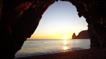 Inside Cave Sunset Ocean Sea View Through Hole. View from the stone cave on the sunset, sea and the beach, the volcanic rock cave lit by warm setting sun. Volcanic basalt as in Iceland. Nobody. video