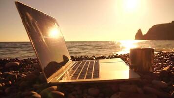 Silhouette of laptop and cup on the beach over sea sunset. Sparkling sea water on background. Freelancer, blogger working on notebook on the beach. video