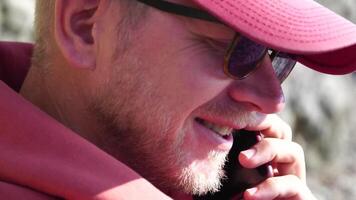 A young man with a beard, dressed in casual clothes smiles while talking on a mobile phone. video