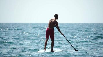 Man Sup Sea. Strong athletic man learns to paddle sup standing on board in open sea ocean on sunny day. Summer holiday vacation and travel concept. Aerial view. Slow motion video