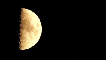Timelapse. A glowing golden half moon as seen from earth through the atmosphere against a starry night sky. A large moon moves across the sky, the moon moving from the left frame to the right. video