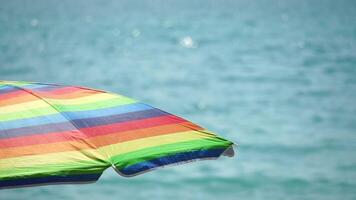 Rainbow colored beach umbrellas or parasols against blue sea during a sunny day on a beach. Symbol of vacations, relax, summer. Colorful umbrellas from the sun stand on the beach. Slow motion. video