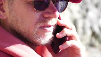 A young man with a beard, dressed in casual clothes smiles while talking on a mobile phone. video