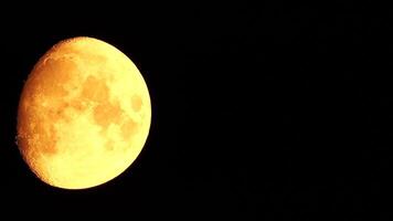 A glowing golden huge moon seen from earth through the atmosphere against a starry night sky. A large moon moves across the sky, the moon moving from the left frame to the right. video
