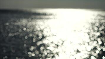 Abstract shining sun reflections on blue surface of sea waves. Bokeh sun glare reflected in water surface. The shimmering small sea waves in sun. Sea on sunny day. Natural bokeh texture. Slow motion video