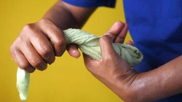 slow motion of Hands squeeze wet towel against yellow background. draining water from wet towel.. video