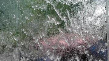 Water is cascading down a glass window, creating mesmerizing and unique abstract patterns video