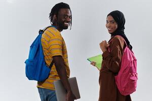 African American student collaborates with his Muslim colleague, who diligently works on her laptop, symbolizing a blend of diversity, modern learning, and cooperative spirit against a serene white photo