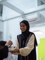 A woman in a hijab extends a platter of dates to her diverse family, creating a scene of unity and joy as they come together to break their fast during the holy month of Ramadan, symbolizing the photo