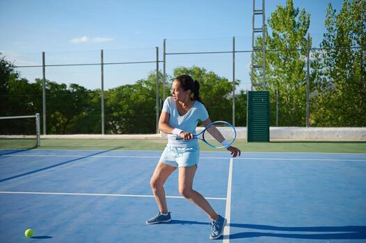 Middle-aged woman playing tennis on an outdoor court on a sunny day photo