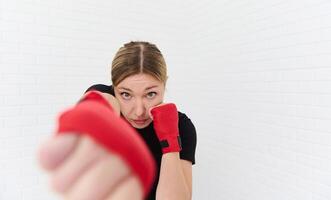 European blonde confident determined female boxer wearing boxing gloves, practicing punching forward the camera, isolated on white background. Blurred fists of hands on the foreground. Copy ad space photo