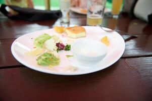 Leftover food on a white plate on wooden table, close-up. Food and drink consumerism. photo