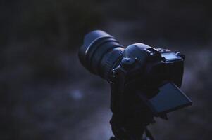 World Photography Day concept. A modern digital semi-mirror camera with a movable touch screen, mounted on a tripod in the nature, ready to take steady shots, pictures, photos or videos.