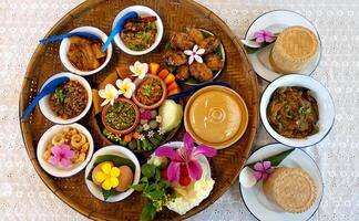 Northern Thai cuisine food set. Pork curry, chilli dip, minced pork salad, soft boiled vegetables and pork snack served in brass dishes. Decorated with flower, garland, spoon and basket background photo