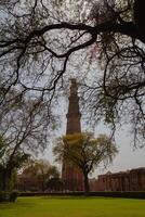 The ancient tower is made of red bricks. There are trees in front photo
