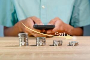 Coins stacking with the down arrow and man using a smartphone to recalculate the cost. Cost reduction concept. photo
