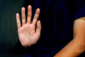 Man giving rejection sign on dark background. Signaling to Stop or refuse something. photo