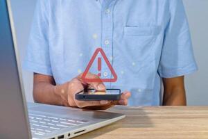 Man holding a smartphone with red triangle caution warning sign for notification error, restricted content or maintenance concept photo