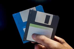 Close up view of hand holding two floppy disks on a dark background photo