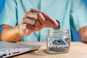 Man working with a laptop and putting coins into a glass jar to prepare for retirement. Saving money for retirement. photo