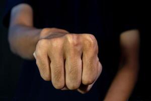 Man with a gesture of clenching his fists forward on dark background. Violence concept. photo