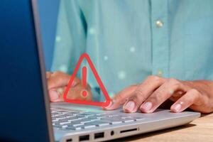 Man using a laptop with red triangle caution warning sign for notification error, restricted content or maintenance concept photo