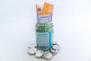 Indonesian Rupiah banknotes in glass jar and scattered coins on white background photo