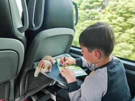 A boy draws in a notebook while sitting on the seat of a passenger bus. The child is traveling by bus and drawing on the way. photo
