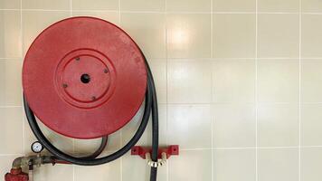 Red fire hydrant reel on a wall waiting for action. A fire pump hose is on a round red sign on the wall indoors. photo