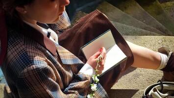 A girl sits sideways on the steps of the university and writes in a notepad. She holds a blooming white branch in her hands. Retro image in the sun's rays photo