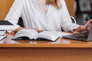 Unrecognizable girl student holding book, making notes at the table, desk in modern university campus library. Education concept, knowledge, wisdom, graduate photo