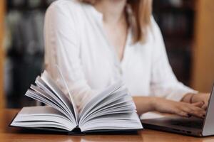 Unrecognizable girl student holding book, making notes at the table, desk in modern university campus library. Education concept, knowledge, wisdom, graduate photo