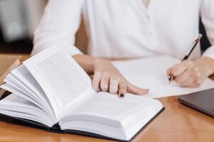 Unrecognizable girl student holding book, making notes at the table, desk in modern university campus library. Education concept, knowledge, wisdom, graduate photo