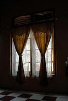 a pair of windows with brown curtains and white lace curtains. The light from outside is shining through the lace curtains, creating a warm and inviting glow in the otherwise dark room photo
