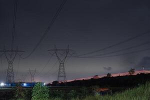 a row of power lines against a dark sky with a long exposure of red light trails in Highways. The power lines are silhouetted against the sky, creating a sense of mystery and intrigue photo