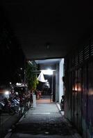 a narrow alleyway at night, with a person sitting on the edge of the sidewalk. The alleyway is dimly lit, and the shadows cast by the buildings and the person create a sense of mystery and intrigue photo