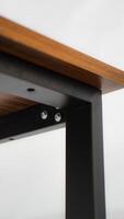 Close-up detail of a wooden table with black metal legs. The image is focused on the junction of the table top and legs, showcasing the sturdy construction and visible screws. photo